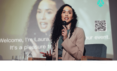 a woman in a suit and a microphone in front of a screen while ohaio livespeaker works