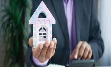Real estate professional holding a small house model while doing calculations.
