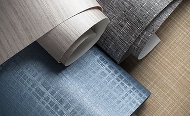 Close-up of textured wallpaper rolls in neutral tan, grey, and blue crosshatch patterns.