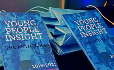 two books with blue covers, and white and black text people, balanced on blue bags on a table