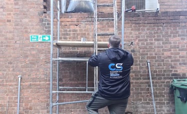 a man in a black shirt is standing on a scaffold fixing ducting at a business premises