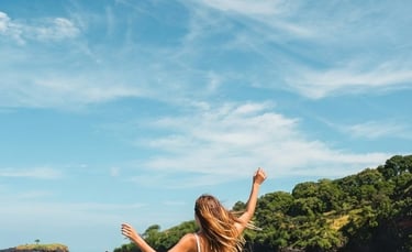 A woman in a flowing white dress stands barefoot on the sandy shore of Virgin Beach, Karangasem, Bali, facing the turquoise s