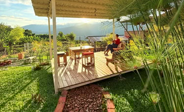 Mujer sentada en una terraza de madera con una mesa y sillas disfrutando del atardecer