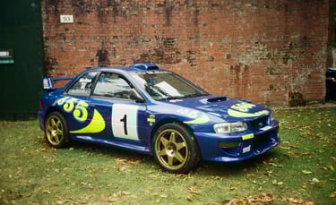 a Subaru Impreza rally car parked in front of a brick building