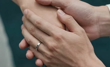 A beautiful close-up of a couple's hands intertwined, focusing on the texture of skin and a wedding ring, set against a dark teal background.