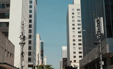 A professional wide-angle shot of a South American city street with modern telecommunications infrastructure and fiber optic cables discreetly integrated into the urban landscape. The scene is bright with natural daylight, featuring a corporate and technological atmosphere in shades of blue and white.
