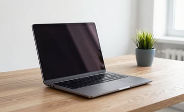 A high-end professional black laptop open on a clean wooden desk in a bright, modern Southern European office. Soft natural light, minimalist setting with a small plant in a grey-blue pot.