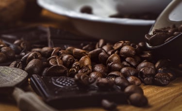 Nahaufnahme von röstfrischen Kaffeebohnen und feiner dunkler Schokolade auf rustikalem Holz