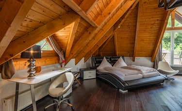 Modernes Hotelzimmer im Dachgeschoss mit gewölbter Holzdecke, Lederbett und stilvollem Arbeitsplatz