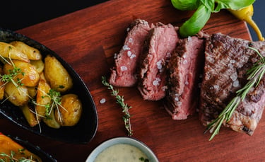 Saftig aufgeschnittenes Rindersteak (Medium) mit Meersalz und Rosmarin auf Holzbrett neben Röstkarto