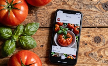 Top-down photography of a rustic wooden table with fresh organic heirloom tomatoes, basil leaves, and a smartphone showing a food profile, South American Brazilian farm-to-table setting, warm natural sunlight, earthy textures, professional and modern style.