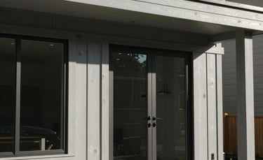 A close-up of a modern residential facade at The Springs featuring pale gray wood panels, large glass windows, and a neat stone porch in a bright North American / US setting.