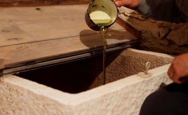 Fresh extra virgin olive oil poured from a red cup into a traditional stone storage vat.