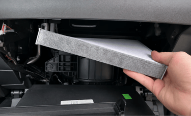 Motorista removendo filtro de cabine do carro durante troca para melhorar a qualidade do ar.