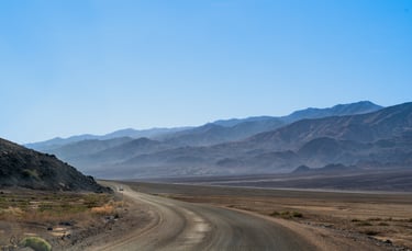 a hazy expanse of mountains intersected by a windy dirt road in death valley california