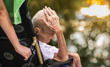 une vieil homme assis dans un fauteuil roulant touche sa tête avec sa main