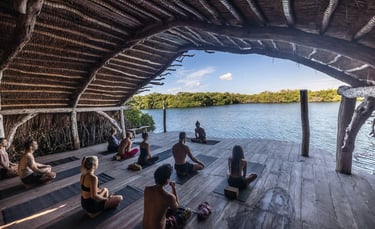People practicing yoga in a wooden pavilion overlooking a serene lake during a yoga retreat.