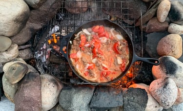 Cast iron skillet over an outdoor fire, cooking chili 