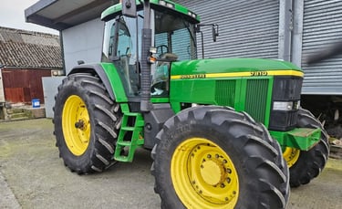 A green and yellow John Deere 7810 tractor parked on a farm beside a metal barn.