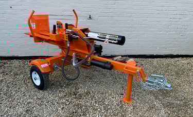 Heavy duty orange hydraulic log splitter machine parked on gravel against a white brick wall.