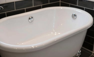 A close-up photograph of a gleaming, high-gloss white porcelain bathtub in a modern New York City bathroom with clean black and white tile accents. The lighting is bright and professional, emphasizing the flawless, smooth surface. Premium industrial aesthetic with soft reflections.