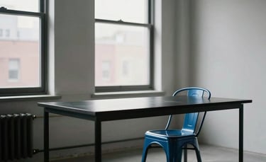 A high-end, minimalist creative studio space in a North American / US city. Large windows with soft natural light, a clean black desk, and a single steel blue designer chair. Professional and quiet atmosphere.