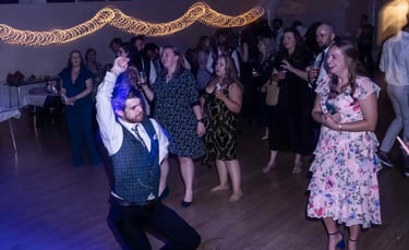 Wedding guests dancing on a wooden dance floor under festive string lights during a lively reception party.