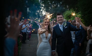 A smiling bride and groom holding sparklers during a wedding send-off celebration with guests.