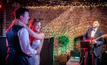 A happy bride and groom enjoy their first dance with a live wedding band in a rustic brick venue.