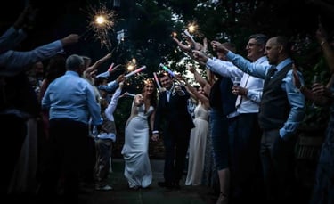 A bride and groom walk through a wedding sparkler send-off celebration at night.