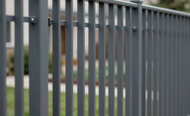 A close-up photograph of a modern grey metal segment fence being installed in a Northern European residential area. The lighting is crisp and natural, highlighting the technical precision and clean lines of the construction. Professional and reliable mood with a neutral color palette including dark grey and surrounding greenery.