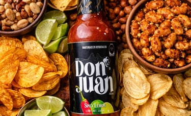 Don Juan Spicy Lemon hot sauce bottle surrounded by chips, guacamole, nuts, and lime wedges.