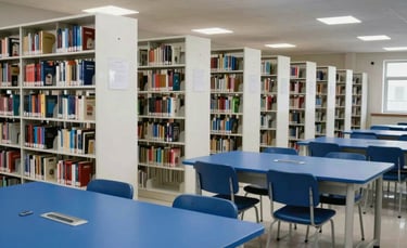 A wide-angle photography shot of a modern Indian school library with white shelving and royal blue study tables. The atmosphere is quiet and professional.