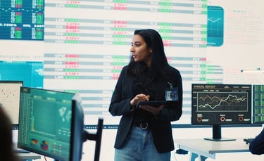 DataOps analyst using tablet in front of a board of data screens