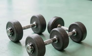 Professional interior photography of a modern North American / US gym space. A set of heavy charcoal grey iron dumbbells rests on a clean, light mint green floor. The composition is clean and minimalist, with bright natural lighting and an energetic vibe.