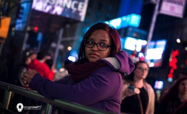 Retrato nocturno de una joven con abrigo morado y bufanda, en Times Square, Nueva York, rodeada de l