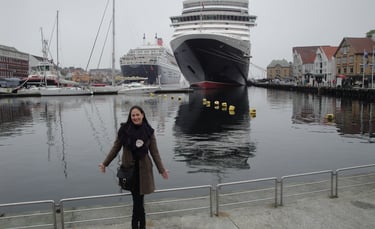 Foto da autora no porto de Stavanger, Noruega — navio Queen Mary ao fundo.