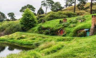 Vista de Hobbiton Village, mostrando as casas temáticas, jardins e paisagens verdes ao redor.