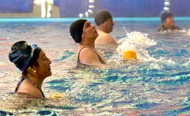 Seniors participating in a water aerobics class at an indoor community swimming pool.