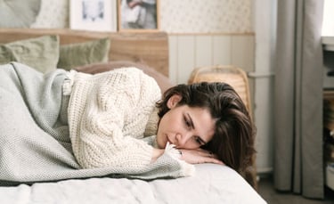 Tired woman lying in bed wearing a knit sweater, looking depressed and lonely at home.