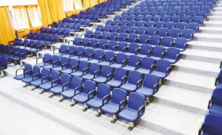 Rows of blue tiered seating in a large empty university lecture hall or theater auditorium.