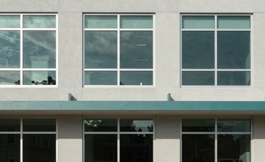 An architectural photography shot of a modern, accessible community building in North America. The facade features large windows and a clean light grey and teal color palette.