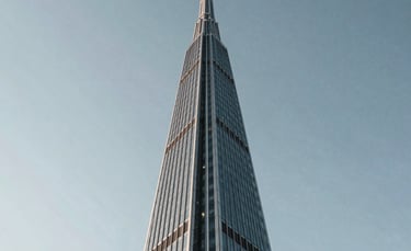 A low-angle shot of a modern glass spire reaching toward a clear sky, symbolizing growth and leadership. The style is professional and minimalist. North American / International architecture.