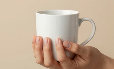 Minimalist close-up photography in a North American home, showing delicate hands with beautifully manicured natural nails holding a warm white ceramic mug against a soft beige background.