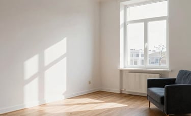 A wide-angle professional photograph of a premium modern apartment interior in Lithuania, featuring clean white walls and natural oak flooring. Soft morning light enters through large windows. Northern European style, minimalist furniture, and impeccable finish quality. Colors include off-white and dark blue-grey accents.