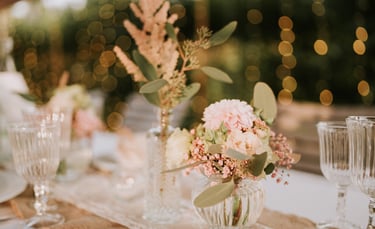 Elegantes Tischgesteck für die Hochzeit mit rosa Blumenarrangements in Glasvasen und warmem Bokeh