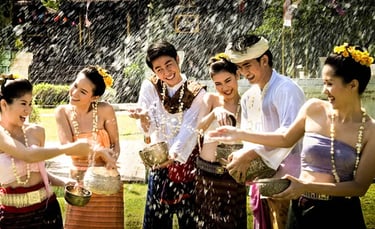 Smiling group in traditional Thai clothing splashing water during Songkran festival celebration.