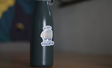 Dark green reusable water bottle with a sheep sticker saying I'm soft but mean to fascists.