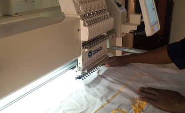 Professional multi-needle embroidery machine stitching yellow thread onto white fabric with a touchscreen control panel.