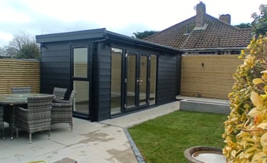 Modern black garden room with french glass doors next to a patio dining set and lawn.